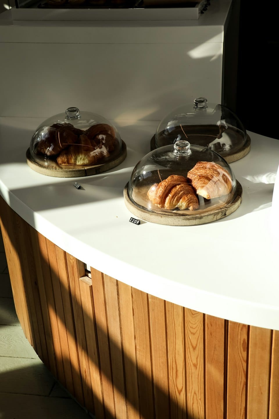 Tre croissant sotto campane di vetro su un bancone da pasticceria.